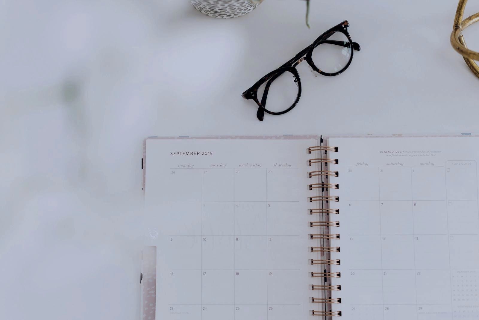 Monthly planner open on a white table next to a pair of glasses.