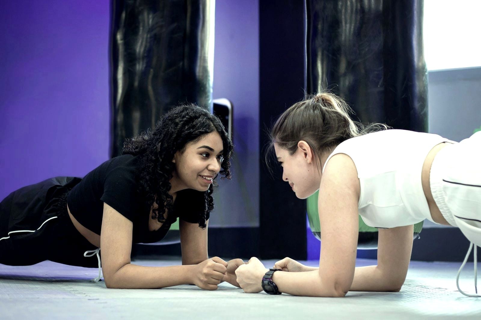 Dos mujeres haciendo plancha frente a frente, sonriéndose.