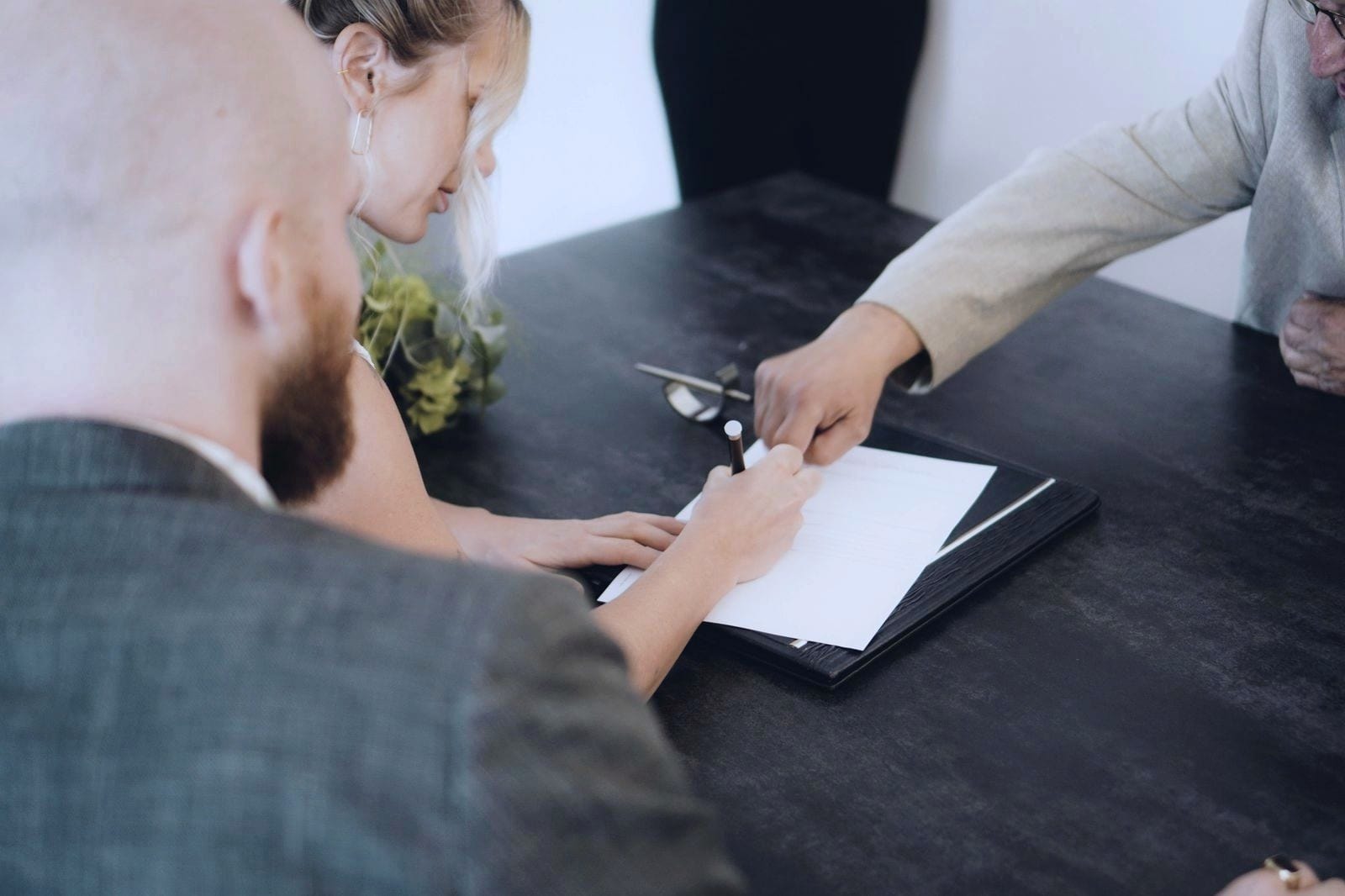 Pessoa a assinar um documento numa mesa enquanto outra lhe indica onde assinar.