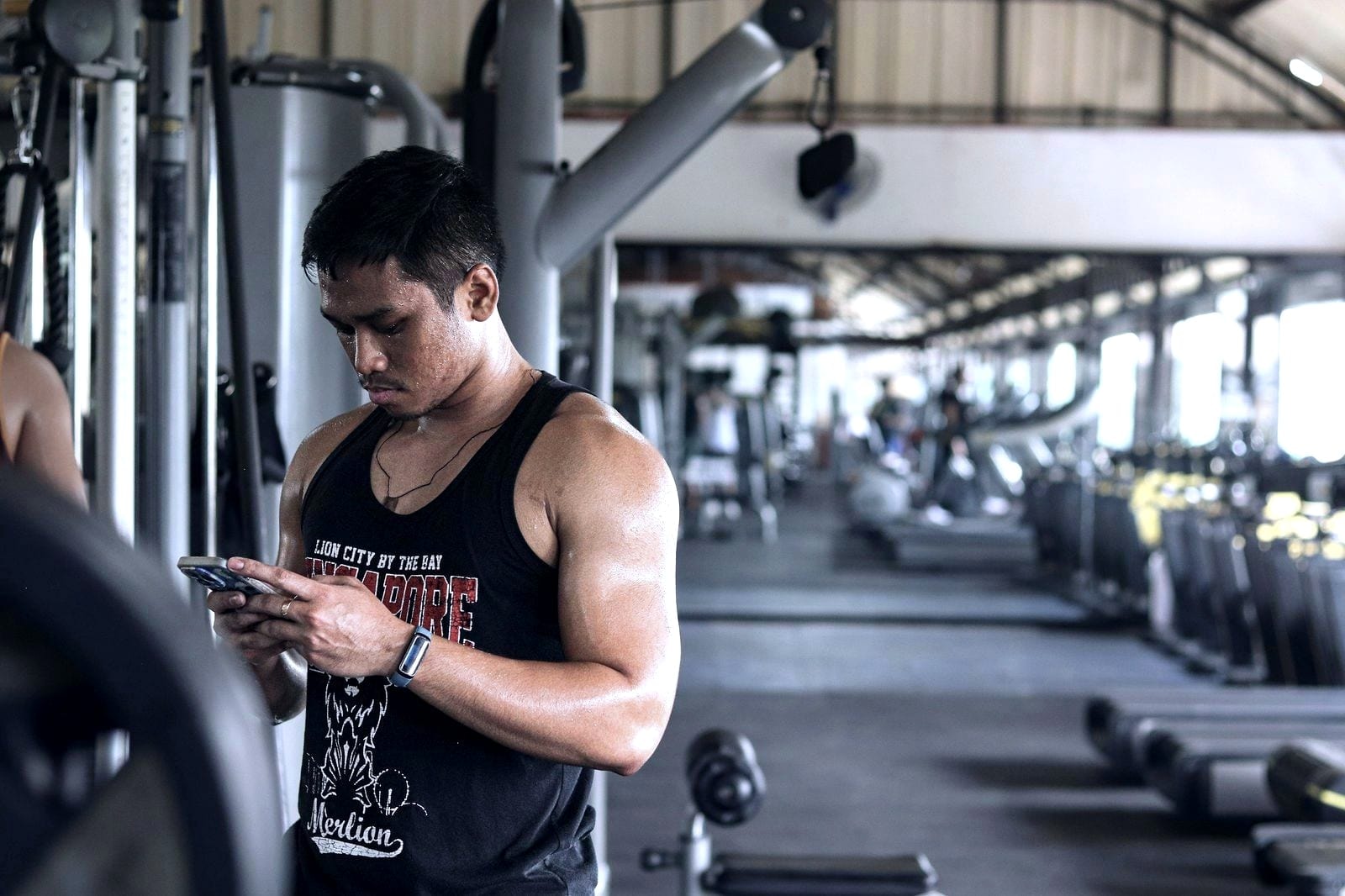 Un hombre en un gimnasio mirando el móvil, con máquinas de entrenamiento detrás.